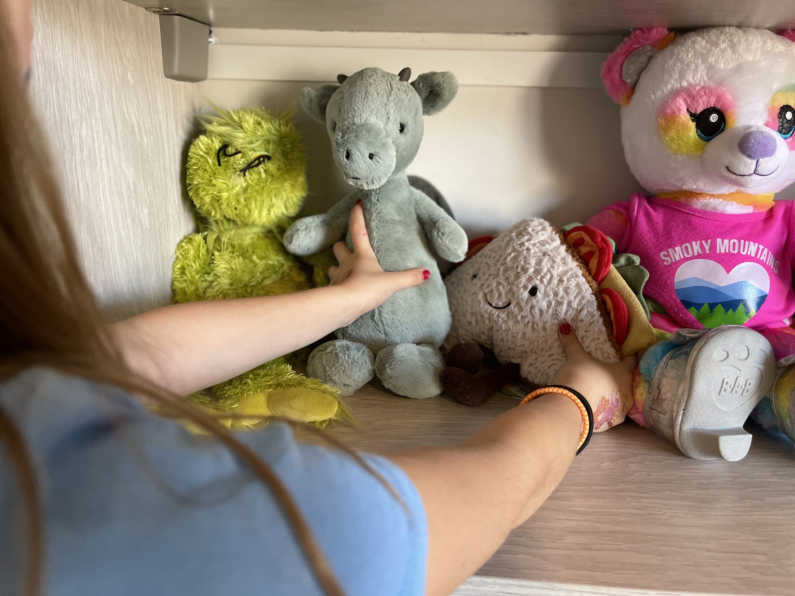 child organizing stuffed animals on toy shelf